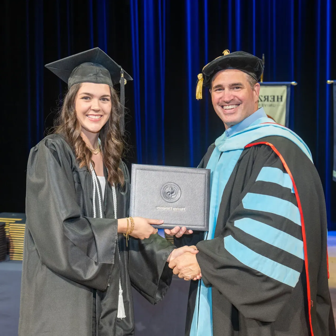 A Herzing University graduate smiling and receiving her diploma during a commencement ceremony, celebrating her academic achievement.